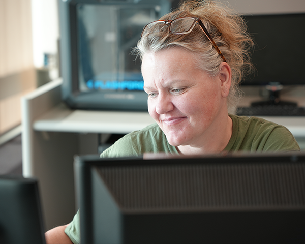 Student smiling while sitting in front of computer and 3D printer in lab