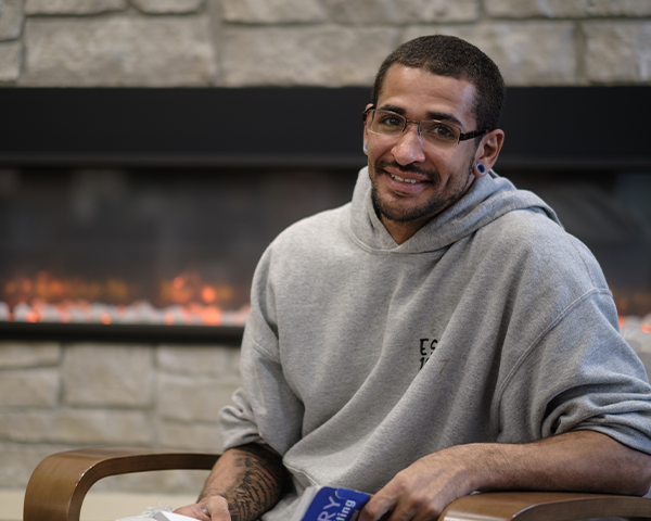 Smiling student sitting in Library lounge space next to fireplace