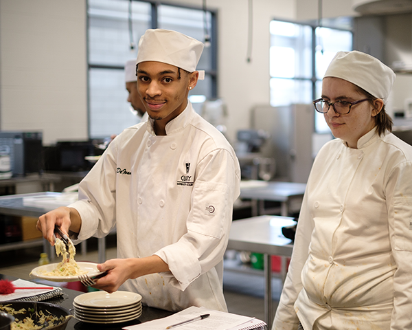 Student serving pasta in chef whites