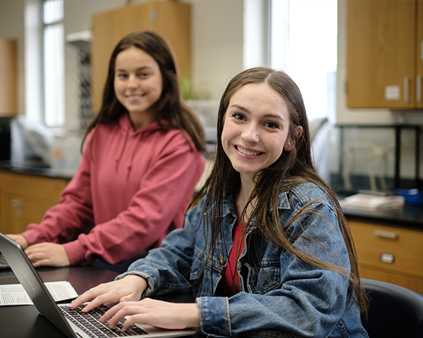 Smiling students working on laptops in lab