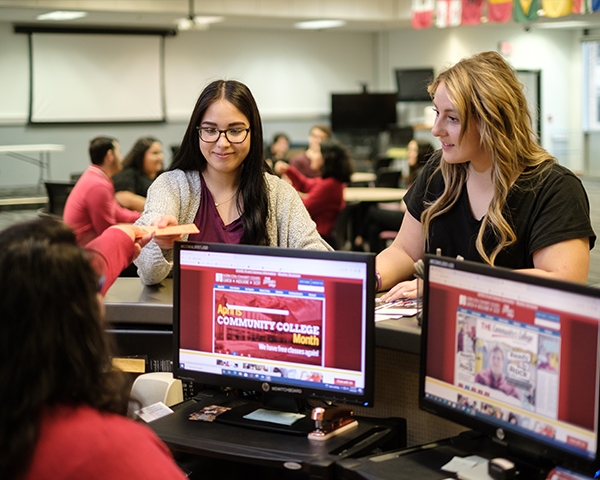 Two smiling female students and information desk