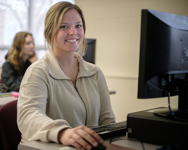 Female student smiling sitting in front of a computer monitor