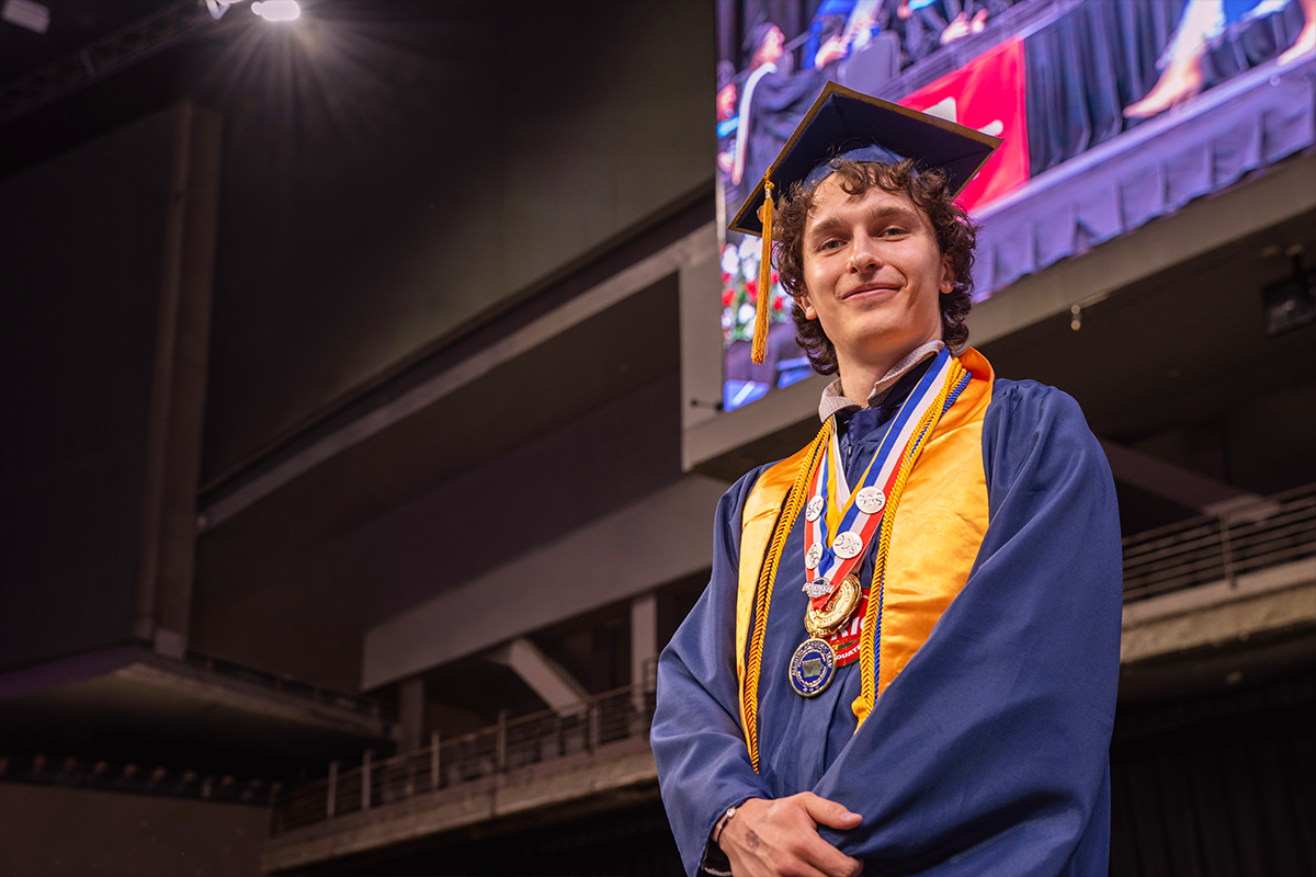 Adam Long in cap, gown and honors standing at podium speaking at Scott's Commencement Ceremony
