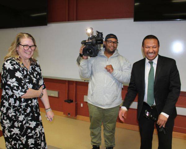 EICC Associate Professor Lori Sheppeard stands laughing in her classroom with a WQAD-TV Channel 8 reporter and a photographer who surprised her with the Pay It Forward Award.